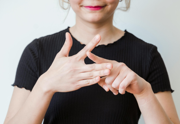 A woman in a black shirt uses American Sign Language, signing with focused hands to communicate in a nonverbal, inclusive way.